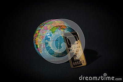 A gold bar and a globe on a black background. The concept of world wealth Stock Photo