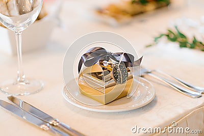 Gold bonbonniere box with a brown satin bow on a serving plate on the Banquet table. Wedding decor Stock Photo