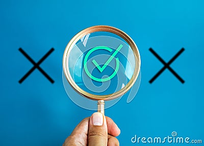 Gold magnifier in hand enlarging and focus on green correct or checkmark icon on blue background. Stock Photo