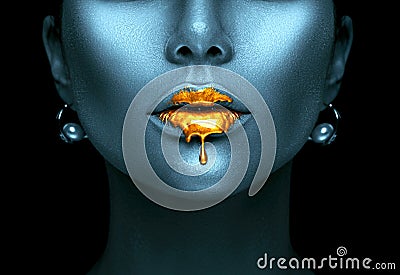 Gold paint drips from the lips, golden liquid drops on beautiful model girl`s mouth, creative abstract dark blue skin makeup Stock Photo