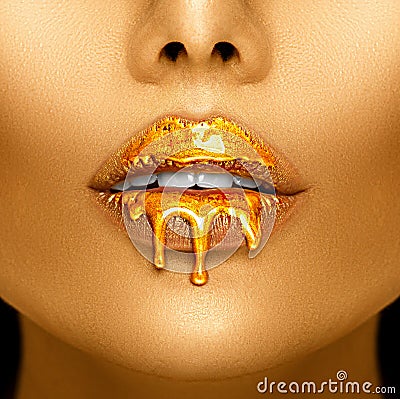 Gold paint drips from the lips, golden liquid drops on beautiful model girl`s mouth, creative abstract makeup Stock Photo