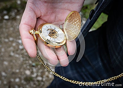 Gold pocket watch with chain open in hand to check time taken outdoor held by man wearing suit on wedding day Stock Photo