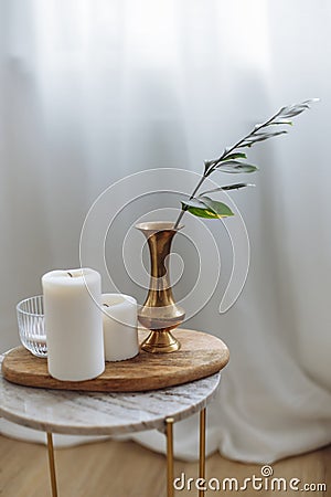 Gold vase with garnish with greens candles marble backsplash wooden board white drapes in cozy scandinavian interior Stock Photo