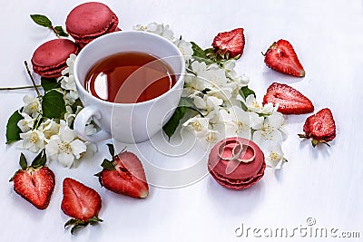 Gold wedding rings beside a Cup of tea, macaroons, strawberries and Jasmine Stock Photo
