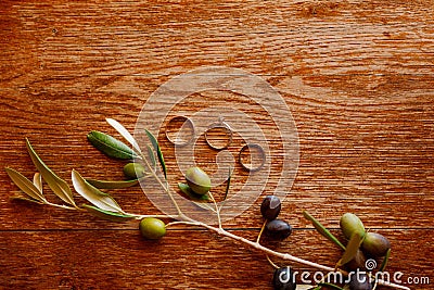 Gold wedding rings and an engagement ring on a brown background with a sprig of olive tree fruits. Stock Photo