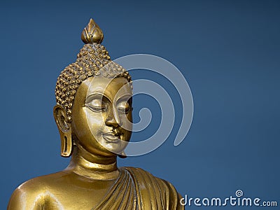 Golden antique buddha statue. The background is light slate gray. The face of the Buddha turned to the right. Stock Photo