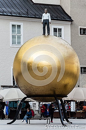 The golden ball statue with a man on the top sculpture, Kapitelplatz Square, Salzburg Editorial Stock Photo