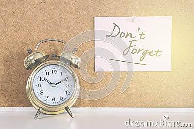 Golden bell alarm clock and a note writen DON`T FORGET on a cork board Stock Photo