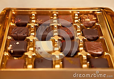 Golden Box of Square Shaped Chocolates in Different Colors and Types Stock Photo