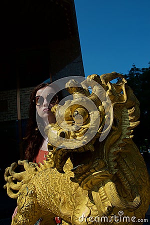 Golden Chinese Dragon Statue with young white female tourist pouting Stock Photo