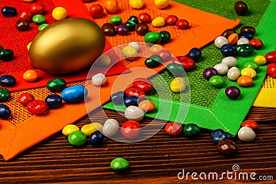 Golden Easter egg with sweets and multicolored napkins on wooden background Stock Photo