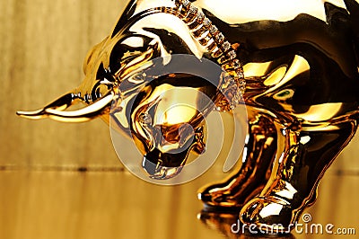 Golden figurine of a bull bowing its head on a gold background close-up. Stock Photo