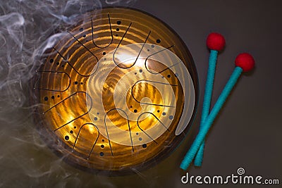 Golden hang drum with blue and red drumsticks with aroma sticks smoke on a black background, top view Stock Photo