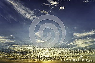 Golden hour sun rays through the beautiful low white scattered clouds on orange blue sky Stock Photo