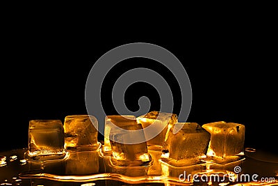 Golden ice cubes on black background isolated closeup, transparent frozen melting amber color water, yellow back light, reflection Stock Photo