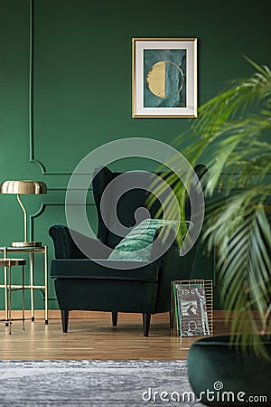 Golden lamp on elegant table next to dark green velvet armchair Stock Photo