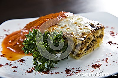 Golden lasagne with meat, tomatoes, cheese sauce and pasta in alternating layers on a wooden board garnished with basil Stock Photo