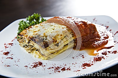 Golden lasagne with meat, tomatoes, cheese sauce and pasta in alternating layers on a wooden board garnished with basil Stock Photo