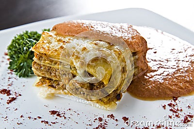 Golden lasagne with meat, tomatoes, cheese sauce and pasta in alternating layers on a wooden board garnished with basil Stock Photo