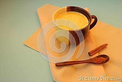 Golden milk in a tan mug, next to turmeric in a spoon and a cinnamon stick Stock Photo