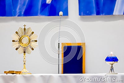 Golden Ostensory or Monstrance for Worship in a Catholic Church Ceremony with a Blue Oil Candle Stock Photo