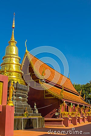 Golden pagoda and brown ubosot with blue sky background Stock Photo