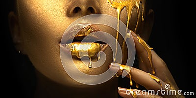 Golden paint smudges drips from the face lips and hand, golden liquid drops on beautiful model girl`s mouth, creative makeup Stock Photo
