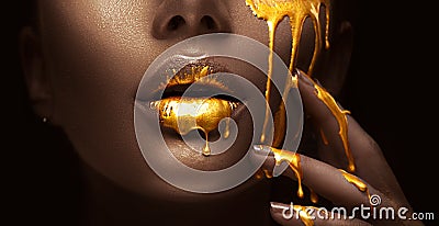 Golden paint smudges drips from the face lips and hand, golden liquid drops on beautiful model girl`s mouth, creative makeup Stock Photo