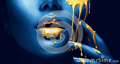 Golden paint smudges drips from the face lips and hand, golden liquid drops on beautiful model girl`s mouth, creative makeup Stock Photo