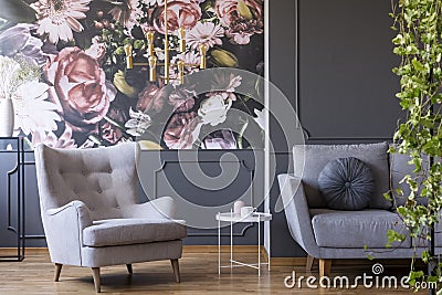 Golden pendant light above a cozy armchair in a fancy living room interior with molding and floral print on gray walls Stock Photo