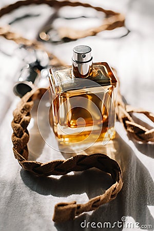 Golden perfume bottle on white fabric background with brown braided leather belt Stock Photo