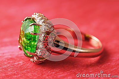 Golden ring with a large emerald and a path of small cubic zirconias on a red abstract background Stock Photo