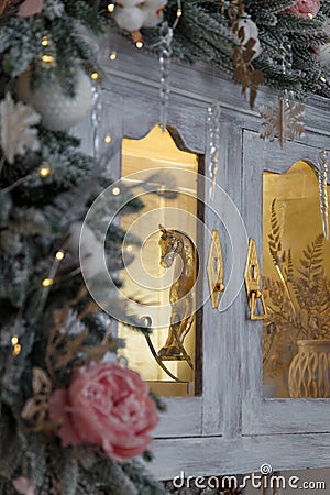 Golden rocking horse toy behind the glass of cupboard, decorated with snowy fir branches and icy roses, snowflakes and icycles Stock Photo