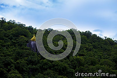 Golden sacred rock at Wat Thewarup Song Tham, Thailand surrounded by forest under the blue sky. Stock Photo