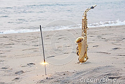 The golden saxophone alto stands on the sand and on the shore, against the background of the sea and Bengal lights. Romantic Stock Photo