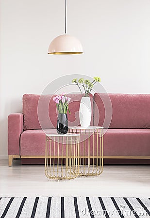 Golden small tables with flowers, pink couch and chandelier in a living room interior. Real photo Stock Photo