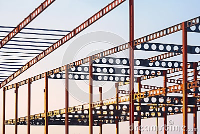 Golden sunlight on surface of red and black castellated beam structure of industrial building in construction site at sunset Stock Photo