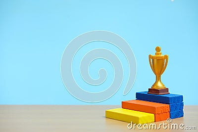 Golden trophy standing at colorful podium on wooden table Stock Photo