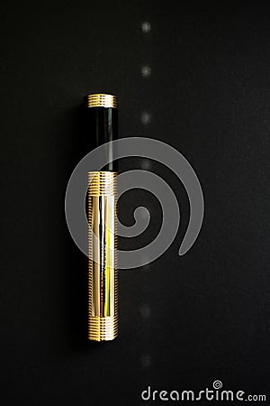Golden tube for mascara, black paper background, glare of light on the background, closed tube of mascara Stock Photo