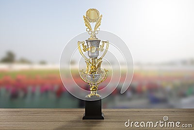 Golden winner trophy cup on wooden table on blurred sport stadium background with crowd Stock Photo