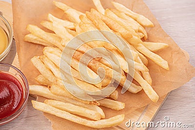 Golden yummy deep French fries on kraft baking sheet paper and serving tray to eat with ketchup and yellow mustard, top view, Stock Photo