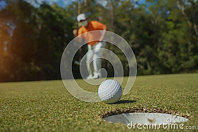 Golfer putting ball on the green golf, lens flare on sun set evening time. Golfer action to win after long putting golf ball in to Stock Photo