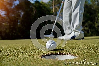 Golfer putting ball on the green golf, lens flare on sun set evening time. Golfer action to win after long putting golf ball in to Stock Photo