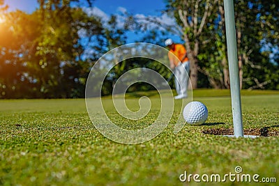 Golfer putting ball on the green golf, lens flare on sun set evening time. Golfer action to win after long putting golf ball in to Stock Photo