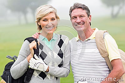 Golfing couple smiling and holding clubs Stock Photo