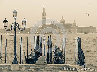 Gondolas moored by Saint Mark square and lamppost with San Giorgio di Maggiore church in the background at foggy day, vintage Editorial Stock Photo