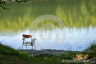 Gone fishing, perhaps, chair left by lake edge. Summer. Background, nobody there in lakeside seat. Stock Photo