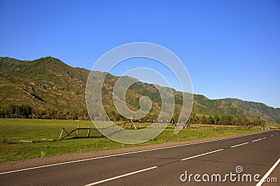 A good asphalt road running at the foot of a green hill along a fertile valley. Landscape Stock Photo