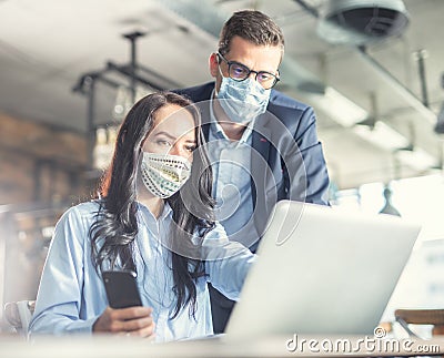 Good looking female and male coworkers look at the computer screen together, wearing face masks Stock Photo