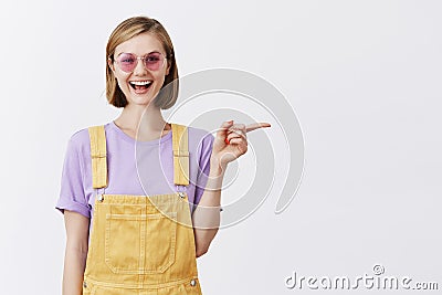 Good-looking friendly and happy female tattoo artist pointing at her room to customer, indicating right with index Stock Photo